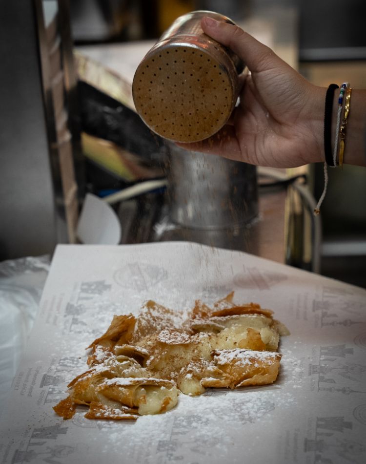 pouring cinnamon over a Greek pastry sweet. 
