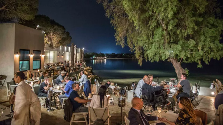 A cozy evening at Ark Restaurant on Glyfada Beach in Athens Riviera, with diners enjoying their meal by the water.