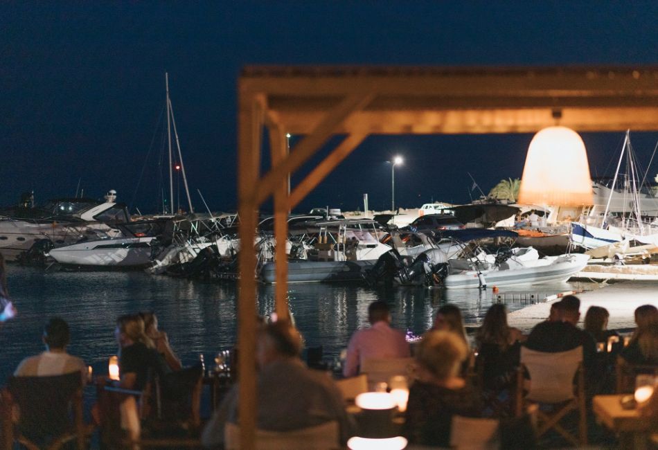 A night scene at Caretta Café in Glyfada, Athens Riviera, overlooking the marina filled with yachts.