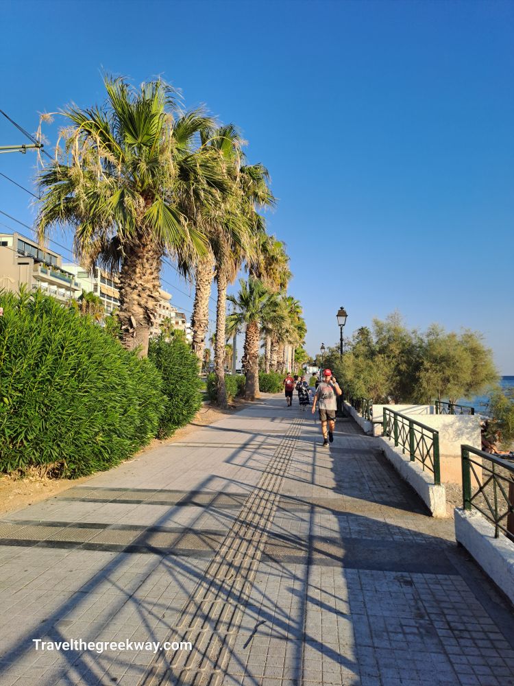 A sunny promenade lined with palm trees, with people walking and enjoying the coastal views.