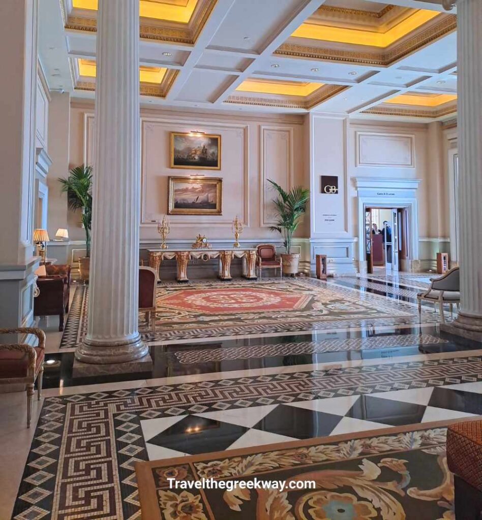 The grand neoclassical lobby of the Hotel Grande Bretagne in Athens, featuring white columns and marble floors.