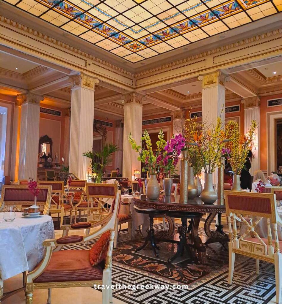 The sunlit Winter Garden at the Hotel Grande Bretagne under a floral stained-glass ceiling.