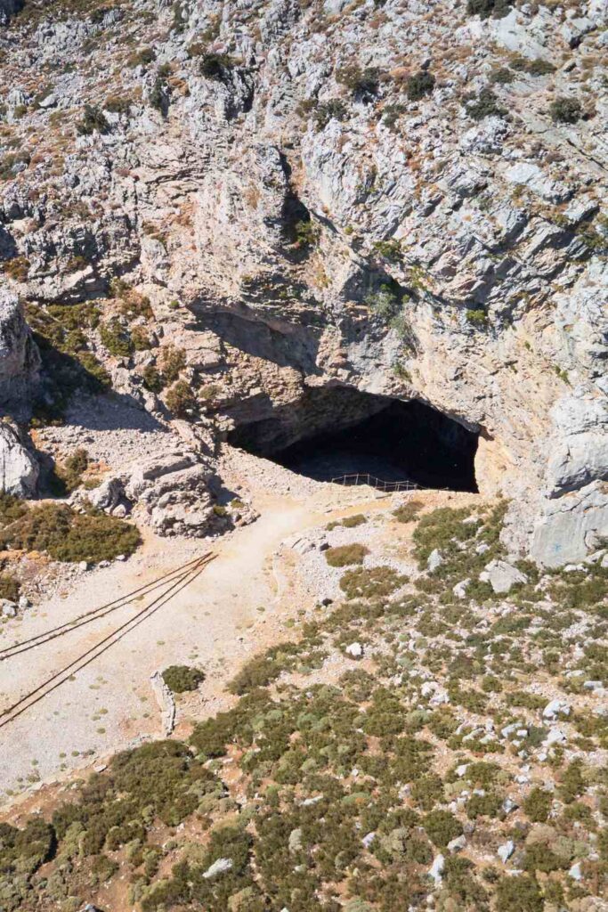 Entrance to the Ideon Cave in Rethymno, Crete, a significant archaeological and mythological site, with rugged rock formations and a pathway leading inside.