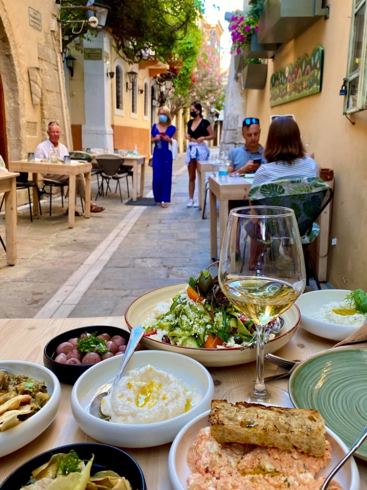 Outdoor dining scene at Avli Tavern in Rethymno, Crete, featuring a table with various Cretan dishes, wine, and diners enjoying their meals in a charming narrow alley.