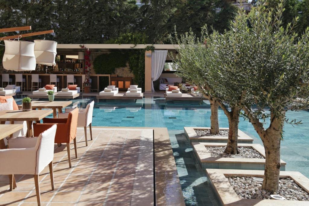 The chic poolside area at The Margi Hotel in Athens Riviera, featuring stylish seating, olive trees, and a luxurious outdoor setting.