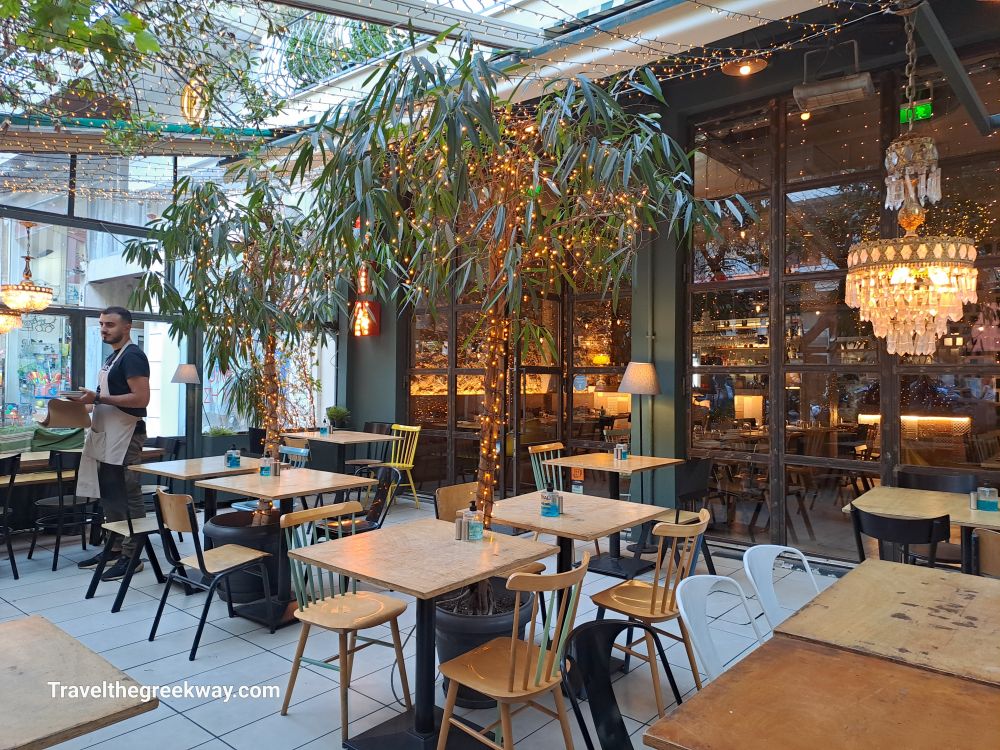  A cozy, well-lit outdoor restaurant in Paleo Faliro with potted plants, hanging lights, and tables set for dining under a clear roof.