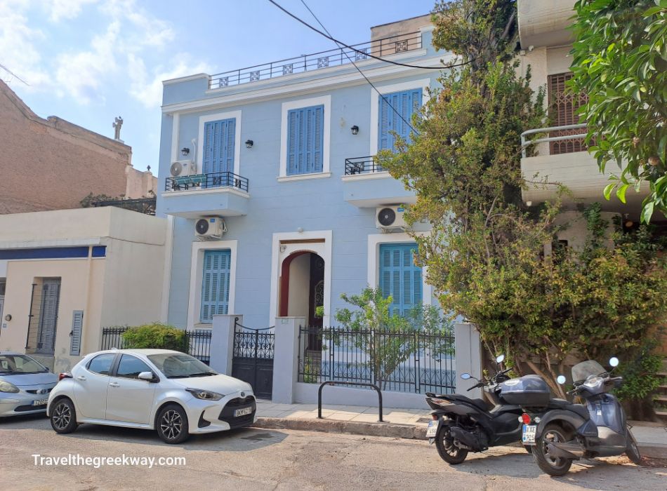 A light blue, neoclassical-style house with shutters and balconies in a residential area of Athens, Greece.