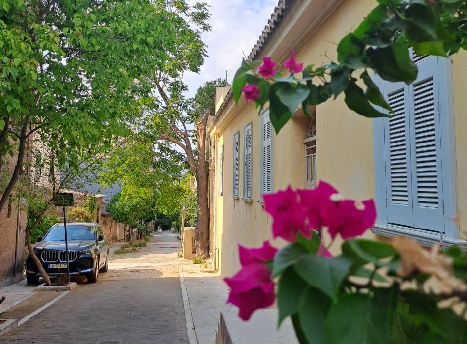 A narrow, flower-filled street in Athens, Greece, with a close-up of pink bougainvillea flowers.