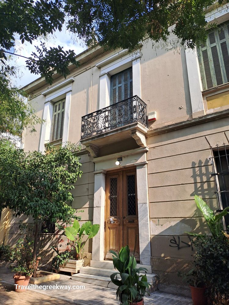 A historic building with a wooden door and balcony, surrounded by greenery in Athens, Greece.