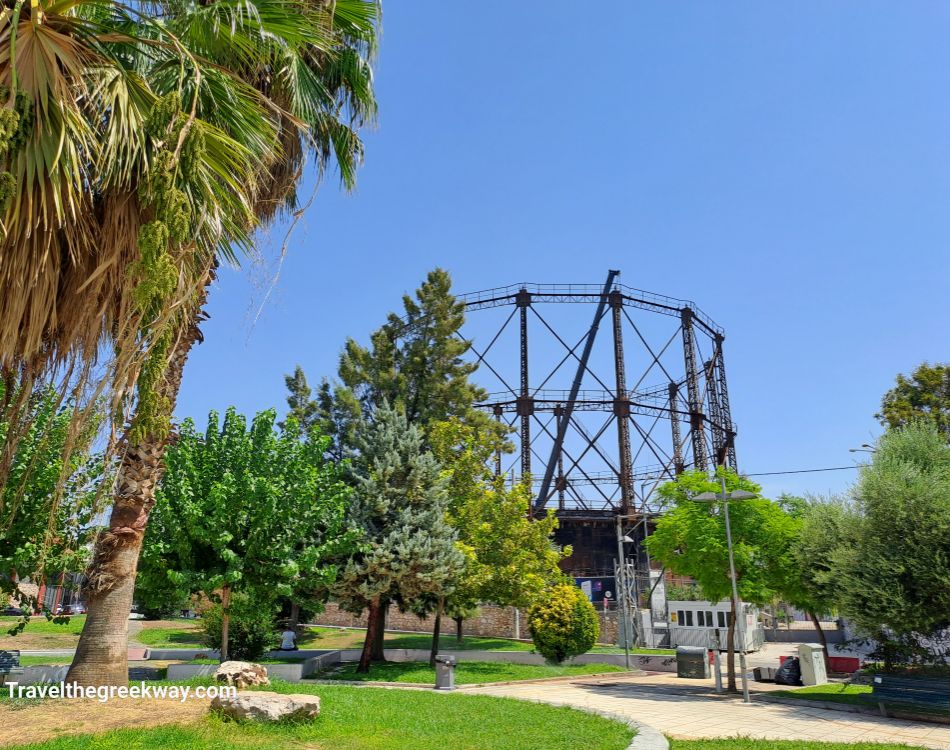 Industrial metal structure surrounded by lush green trees and palm trees in a park in Athens, Greece.