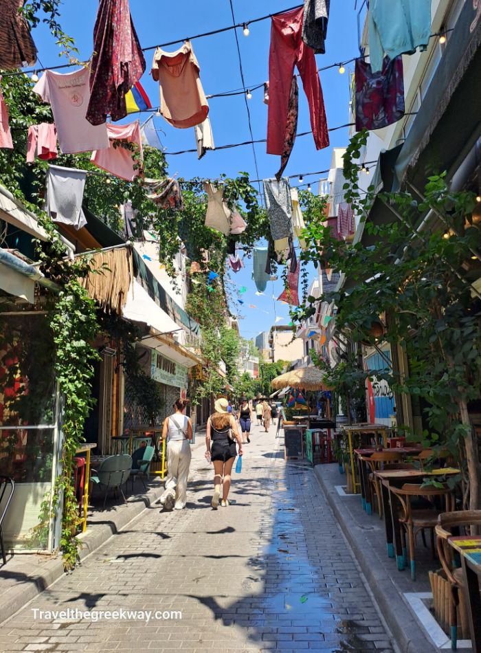 A vibrant street in Psiri, Athens, decorated with colorful clothes hanging above, with small shops and cafés along the walkway.