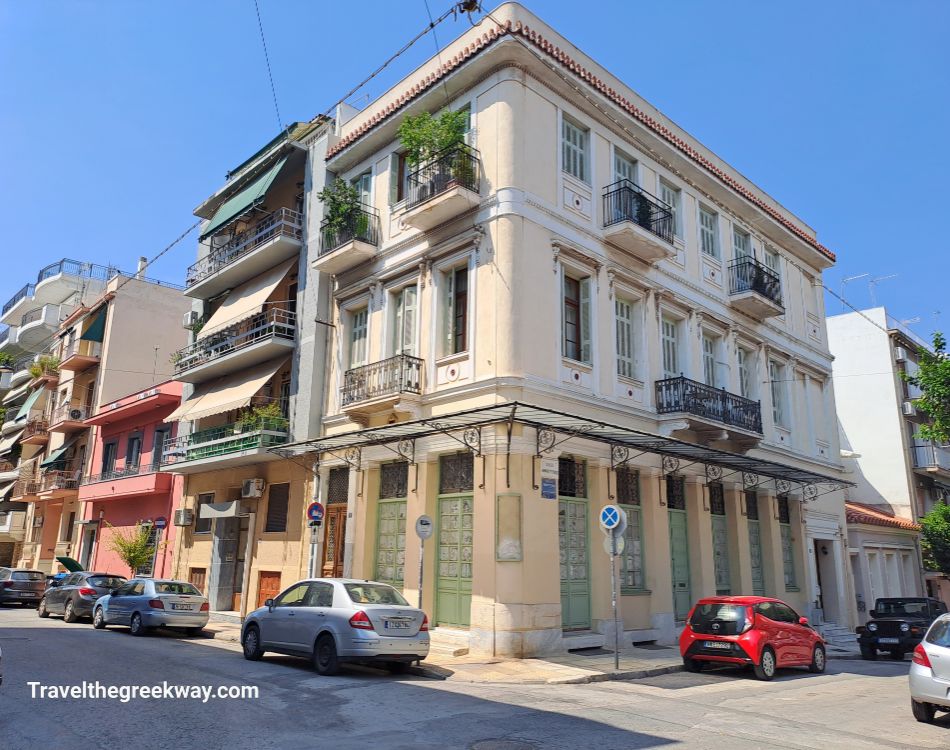 Corner view of a neoclassical building with balconies and large windows in Athens, surrounded by modern and traditional buildings.