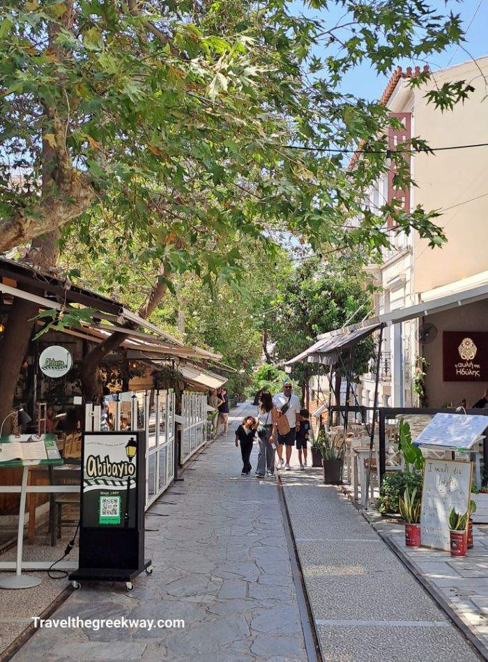  A quiet street in Thissio, Athens, lined with trees and outdoor cafés, creating a relaxed atmosphere for visitors.