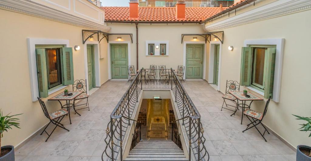 Interior courtyard of a traditional Athenian guesthouse with green shutters and outdoor seating on the upper level.