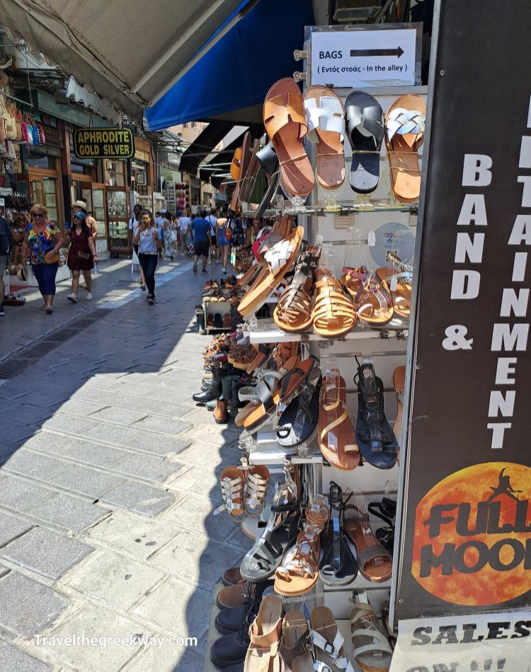  A display of traditional leather sandals for sale at Monastiraki Flea Market in Athens, with shoppers browsing the market stalls.