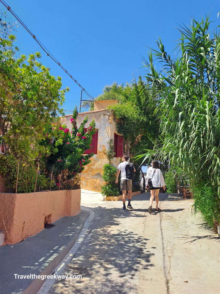 Charming alleyway in Plaka, Athens, with lush greenery and tourists exploring under a clear blue sky.