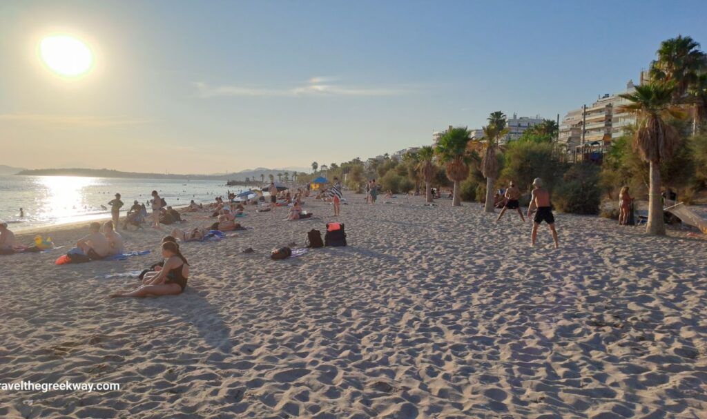 Sunbathers and beachgoers enjoying the late afternoon sun on Edem Beach, with a beautiful view of the sea and palm trees lining the shore.