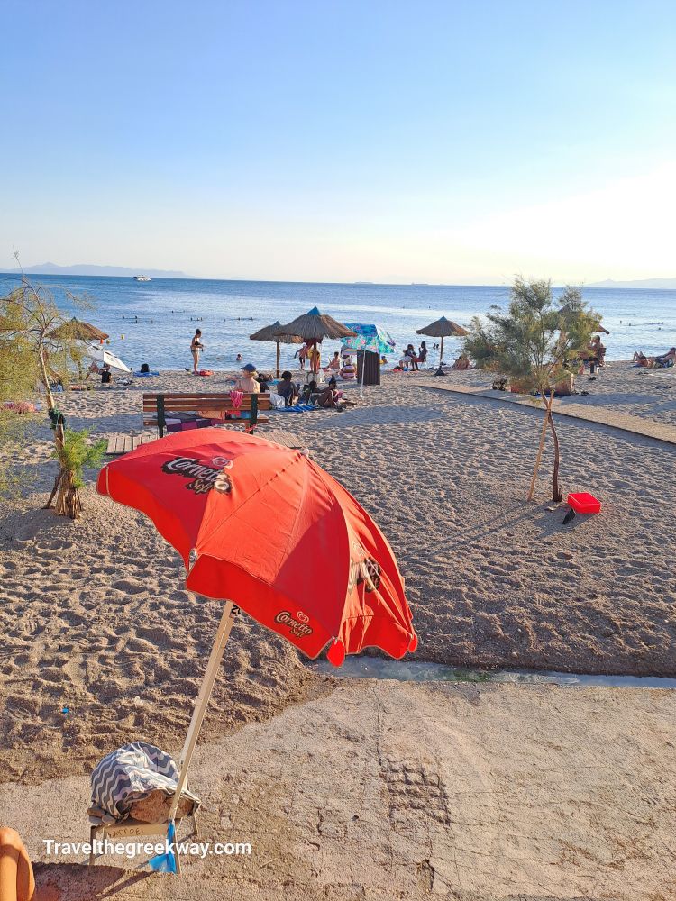 Red umbrella on Faliro Beach, with beachgoers and a clear blue sea under the sun.