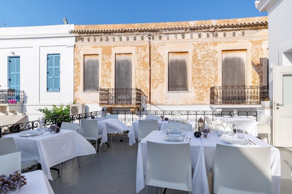 Elegant outdoor dining area on a terrace in Paros, Greece, with views of traditional buildings.