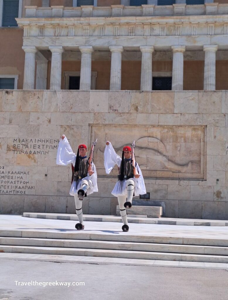 The Evzones, ceremonial guards, perform in front of the Hellenic Parliament in Athens, with the iconic building as the backdrop.