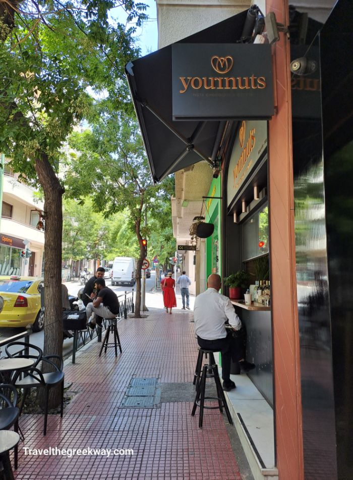 A lively street in Kolonaki, Athens, lined with cafés where people are sitting and enjoying the shaded outdoor seating.