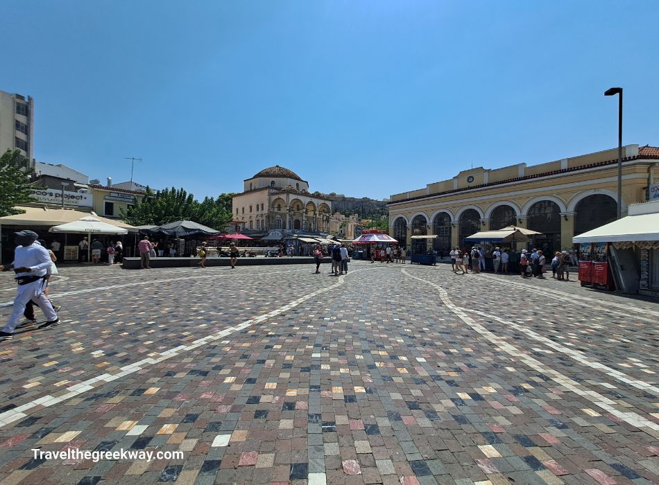 Monastiraki Square in Athens, bustling with activity and surrounded by historic buildings and market stalls on a sunny day.