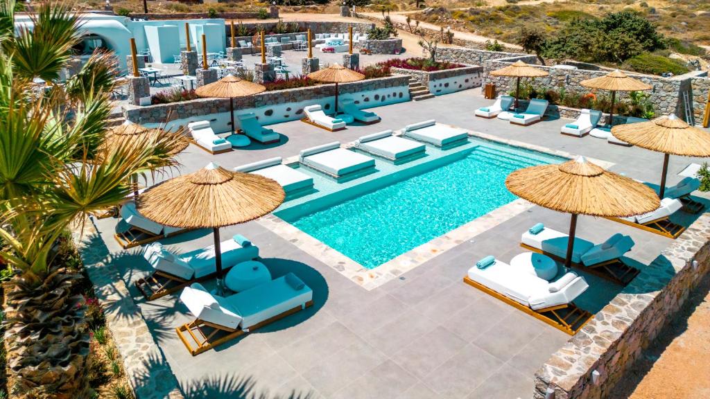 Luxury outdoor pool area at Naxos Cave Suites, featuring sun loungers with straw umbrellas, surrounded by a serene landscape.