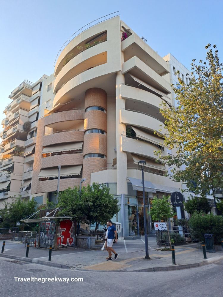 A contemporary multi-story building with curved balconies and a street-level cafe in Paleo Faliro, Athens Riviera.