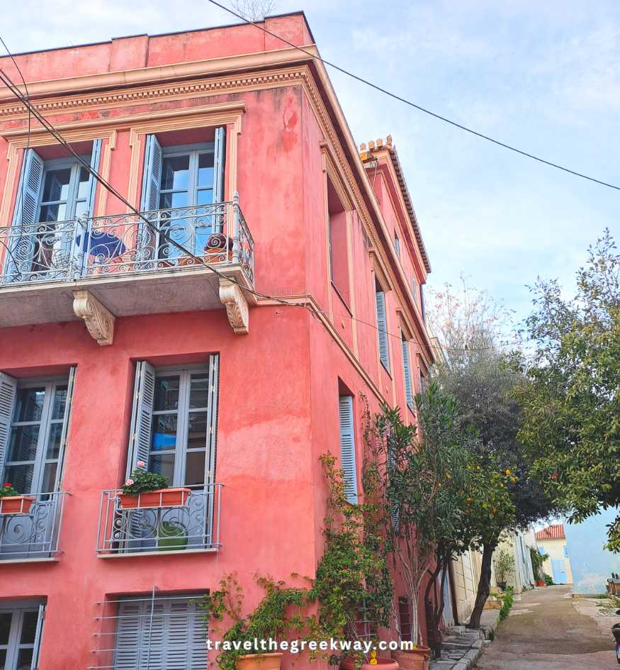 A bright pink neoclassical house with blue shutters and decorative balconies in Plaka, Athens.