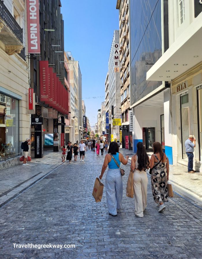  A busy day on Ermou shopping street in Athens, with shoppers walking along the pedestrianized area, surrounded by retail stores.