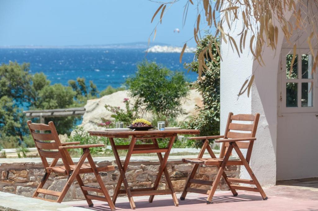  A peaceful outdoor dining area with wooden chairs and a table overlooking the sea, surrounded by greenery in Naxos Greece.