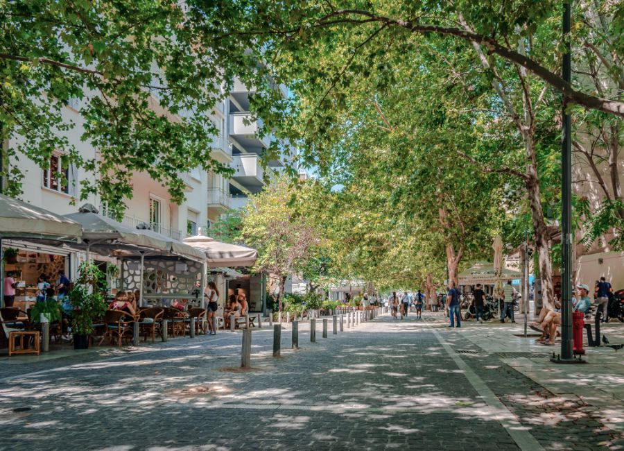 A peaceful view of Dionysiou Areopagitou Street, Athens, with the Acropolis in the background and trees lining the pedestrian path.