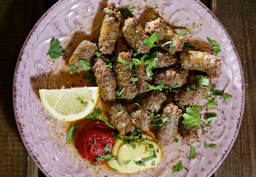 Plate of traditional Greek sausage garnished with parsley and served with lemon and dipping sauces.