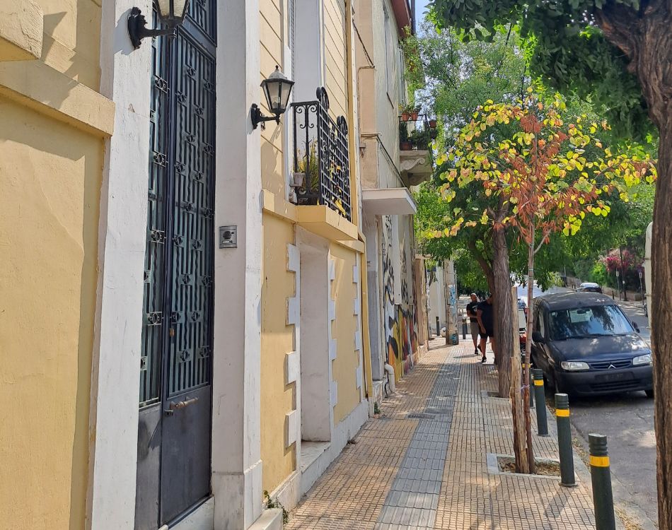 A quaint, tree-lined street in a residential area of Athens with yellow-painted buildings.