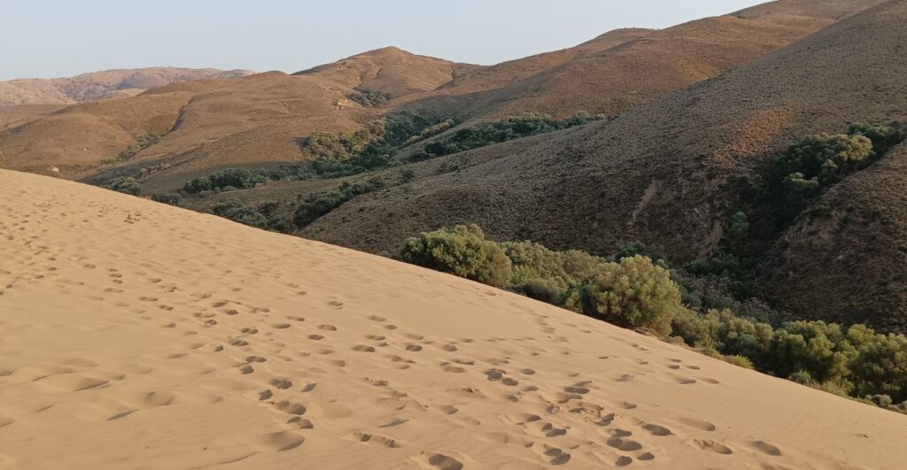 Expansive view of the sand dunes in Lemnos, with footprints marking the soft sand and green valleys in the background.