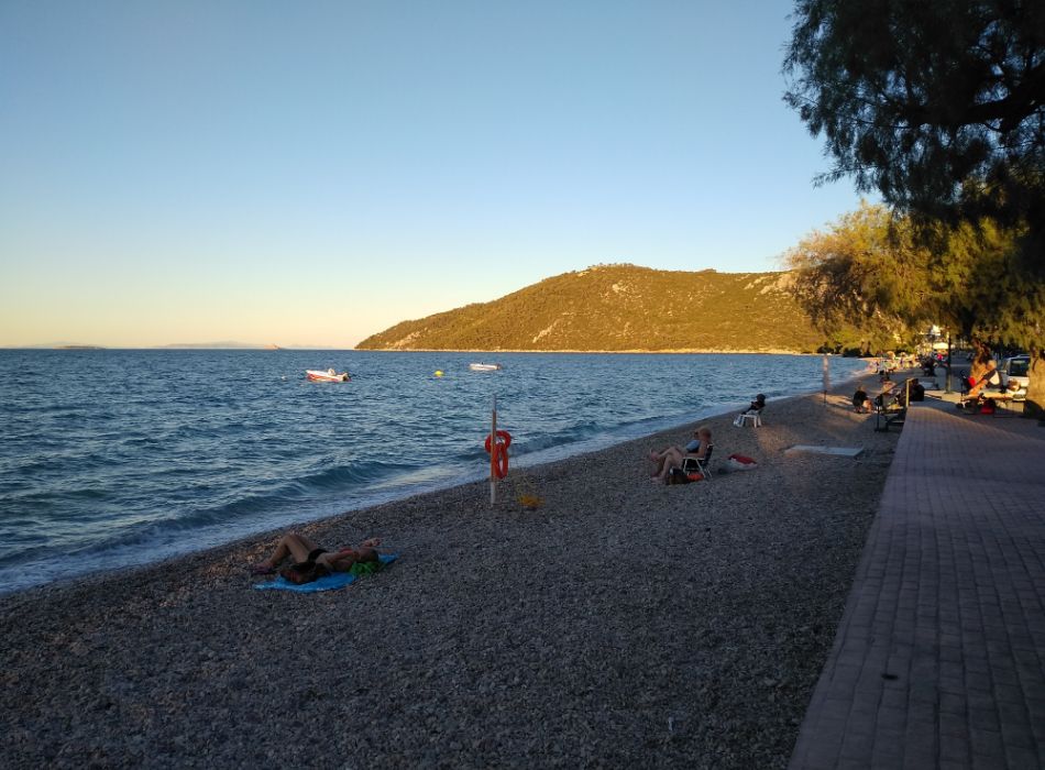 Quiet beach at Loutra Oraias Elenis in Peloponnese, Greece, with calm waters and people relaxing by the shore.