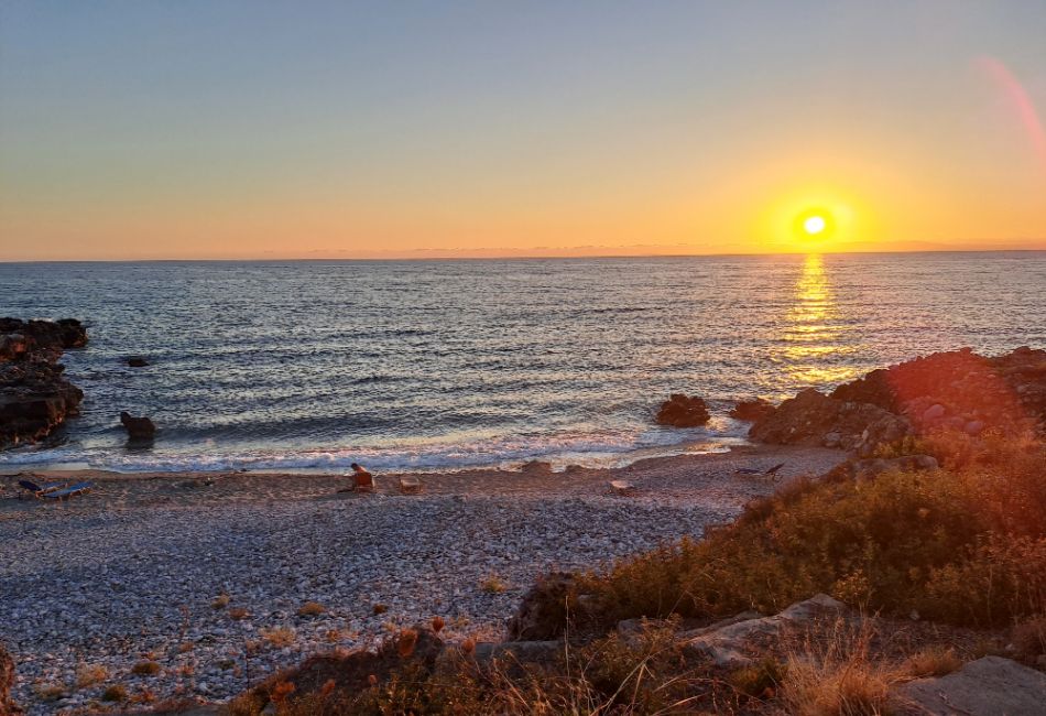 Stunning sunset view over a rocky beach in Peloponnese, with golden light reflecting on the sea