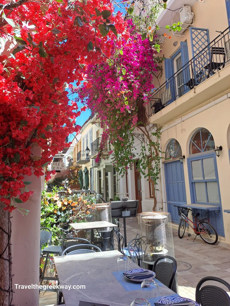 Colorful street in Nafplio, Greece, adorned with vibrant bougainvillea and charming outdoor seating.