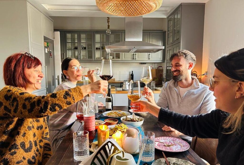 Friends enjoying a culinary experience at a cozy table, toasting with wine and sharing Greek dishes.