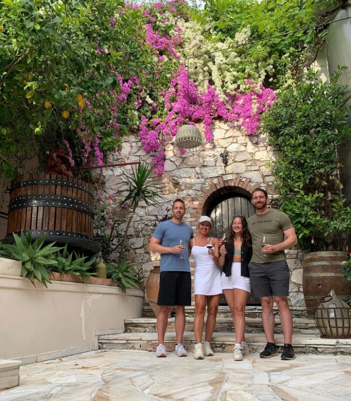 Group enjoying a wine tasting in a beautiful courtyard adorned with lush bougainvillea and stone walls.