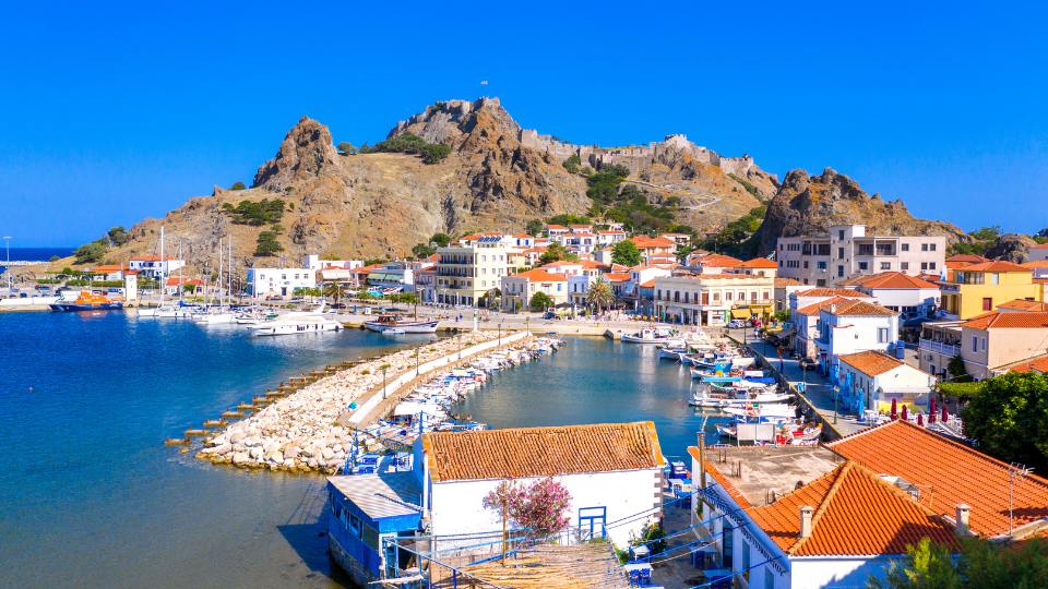 View of Myrina's picturesque harbor with boats docked, charming buildings, and the Venetian castle on the hilltop.