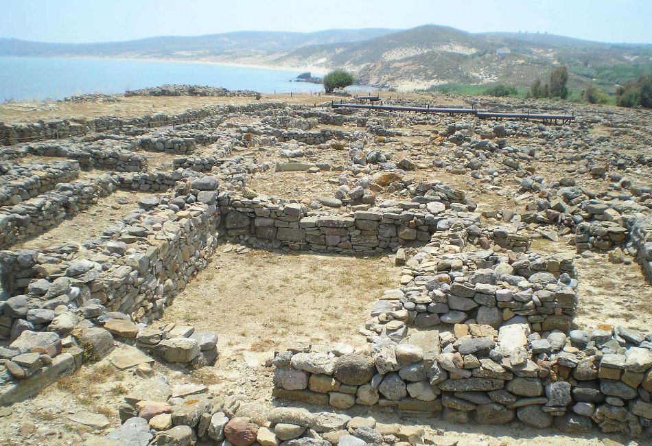 Ruins of the ancient settlement of Poliochni, overlooking the sea, showcasing stone foundations and walls.