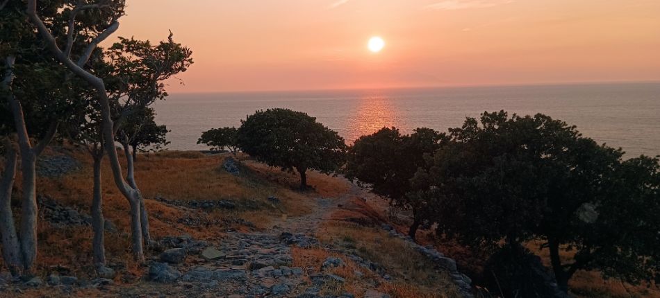 Stunning sunset view from Myrina Castle, overlooking the sea with trees silhouetted against the orange sky.