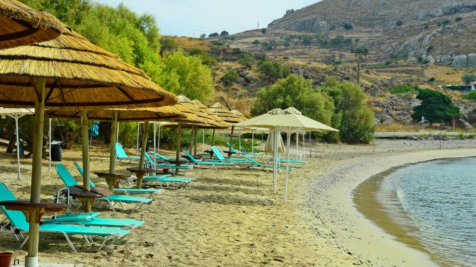 Agios Ioannis Beach in Lemnos with straw umbrellas and sun loungers lining the sandy shore.