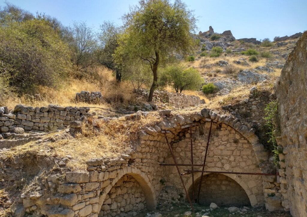 Stone ruins with arched supports amidst natural greenery at Acrocorinth, Ancient Corinth.