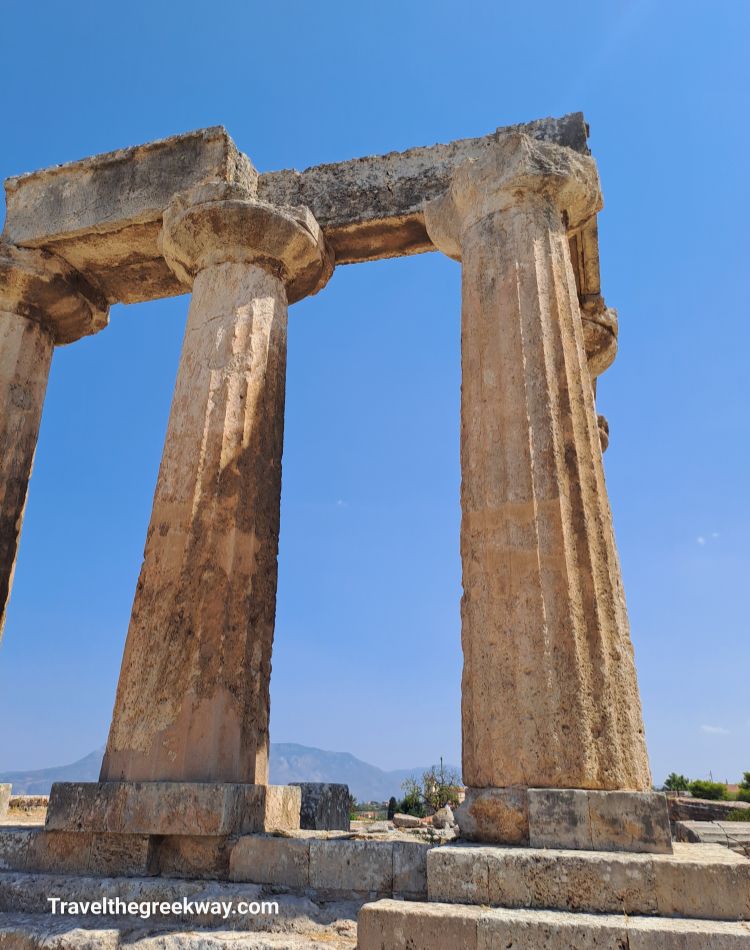 Close-up view of the towering stone columns of the Temple of Apollo in Ancient Corinth against a clear blue sky.