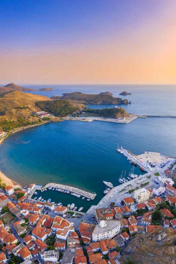 Aerial view of Lemnos port at sunset with boats docked and orange-roofed buildings surrounding the harbor.