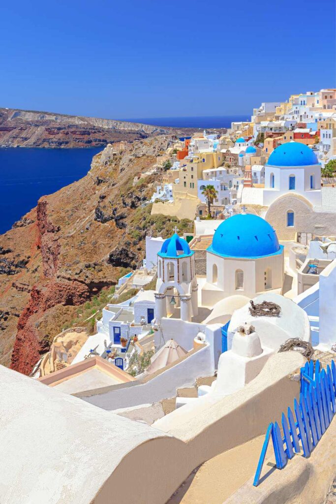 Iconic blue-domed churches and whitewashed buildings overlooking the sea in Santorini. Which Greek Island Are You? 