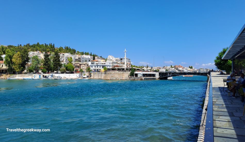 Seaside promenade in Chalkida, Greece, with blue waters, a bridge, and a charming town in the background.