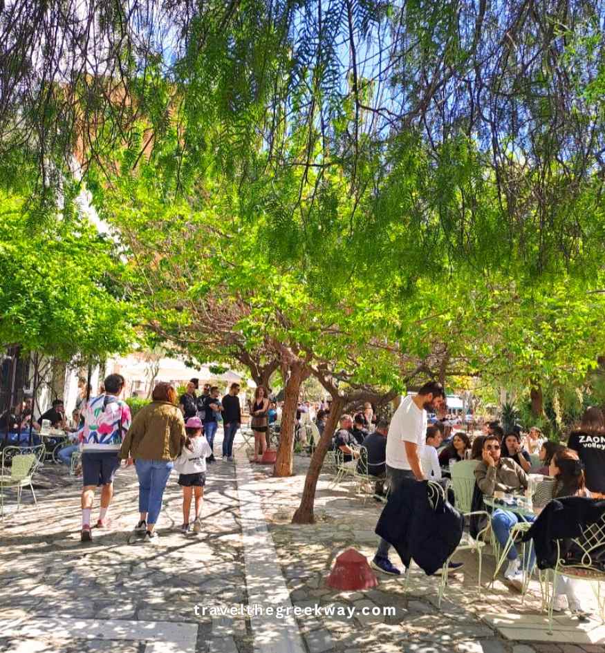 Locals and tourists enjoying coffee and food at an outdoor café shaded by trees in the neighborhood of Metaxourgio, Athens.